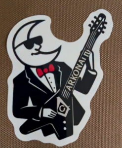 Tuscan Travellers commemorative logo featuring a stylized figure in formal attire playing a guitar labeled Arkona, representing their visit to Arkona Lodge No. 307