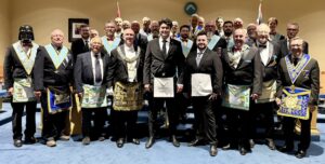Group of Freemasons in formal attire and aprons gathered inside a lodge room after a ceremony.
